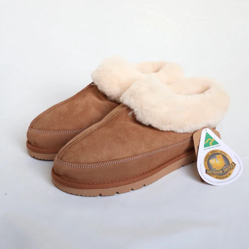 Brown suede slippers with white fur lining on a light gray background, featuring a brand tag.