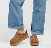 Close-up of feet wearing brown shoes with red soles and blue jeans.